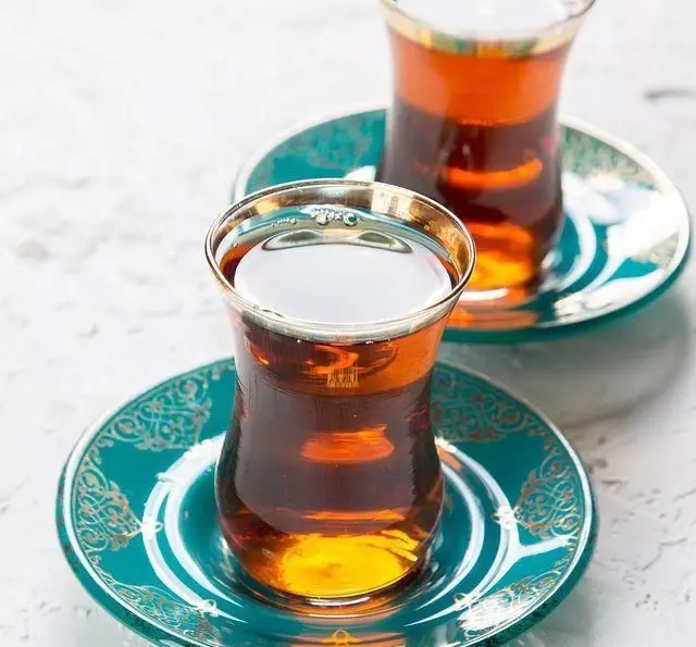 دو استکان چای عربی خوش‌رنگ و سنتی با نعلبکی‌های فیروزه‌ای و طرح‌های طلایی در کافه رستوران عربی مدائن، بهترین نوشیدنی.