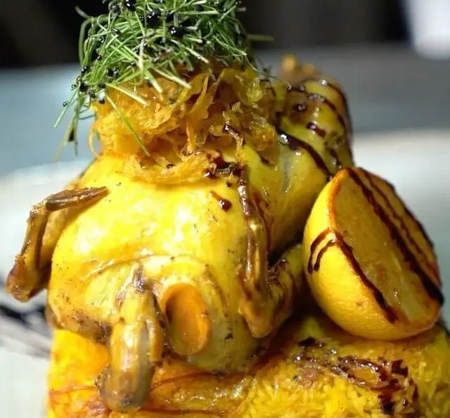 مرغ کامل زعفرانی و برشته با تزئین پیاز برشته و سبزیجات تازه، روی پلو، در کافه رستوران عربی مدائن، یک غذای سنتی لذیذ و دلپذیر.