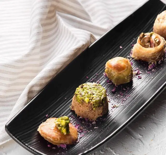 سینی از شیرینی‌های اصیل عربی کافه رستوران مدائن، شامل انواع باقلوا و دسرهای سنتی با پسته و گل محمدی.