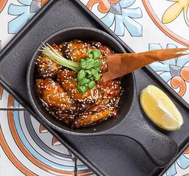 بال مرغ گلازه‌شده با کنجد فراوان، برگ ریحان و لیموی تازه، از منوی پرطرفدار کافه رستوران عربی مدائن. غذایی خاص.