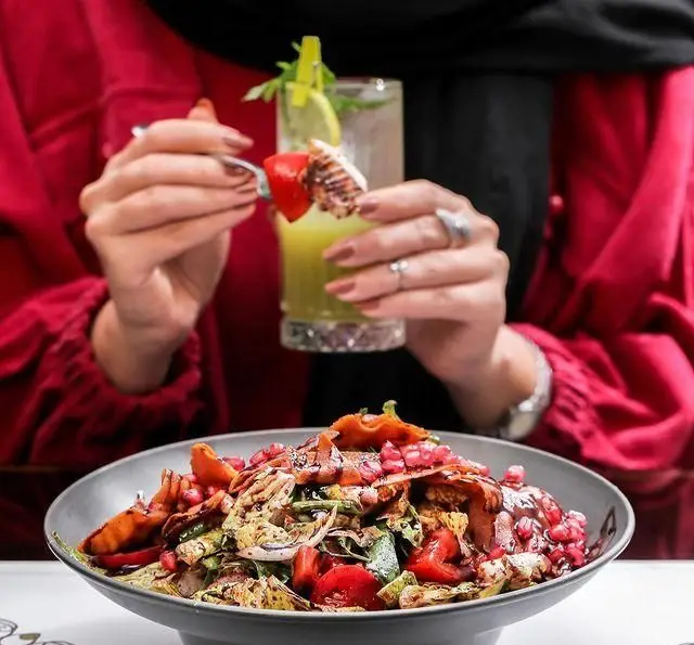 تجربه دلپذیر غذاخوری در کافه رستوران عربی مدائن: لذت بردن مشتری از سالاد فتوح غنی با جوجه گریل و نوشیدنی گوارا.