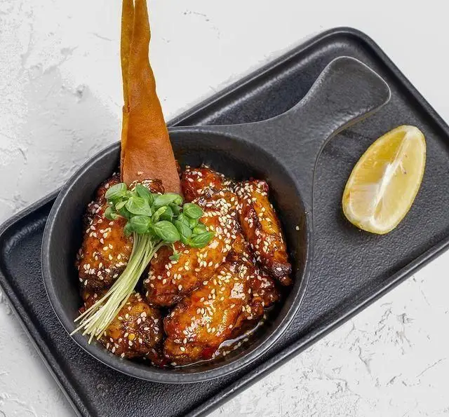 بال مرغ کنجدی گلیز شده با سس مخصوص و تزئینات سبز، سرو شده به همراه لیمو در کافه رستوران عربی مدائن. طعم اصیل و لذیذ.