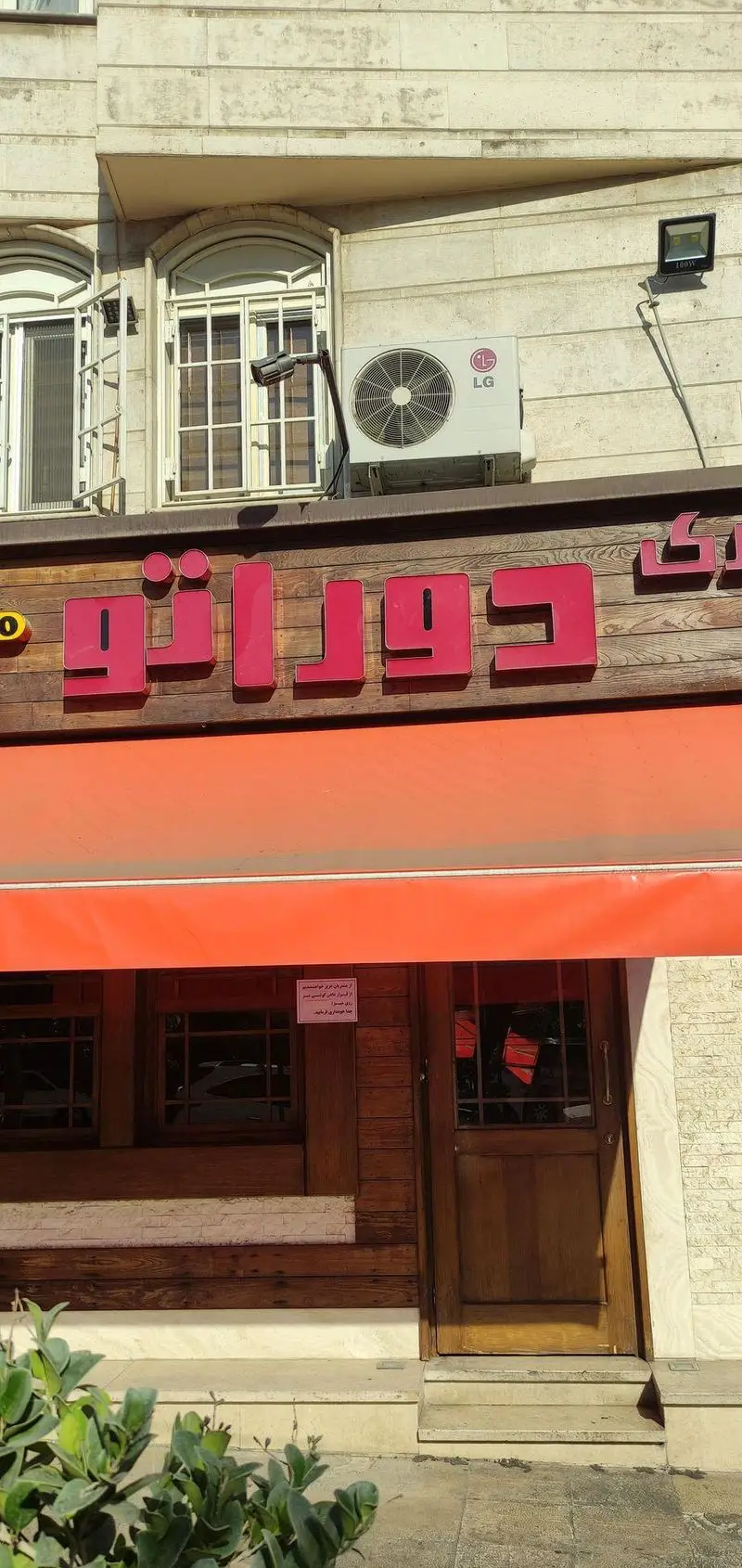 ورودی فست فود دوراتو، با تابلوی قرمز رنگ "دوراتو" روی زمینه چوبی، سایبان نارنجی و درب چوبی رستوران.