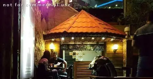 فضای دلنشین و دنج رستوران پیتزا سیب ۳۶۰ در شب. مشتریان در محیط باز زیر سقف نارنجی شام می‌خورند، با نورپردازی گرم.