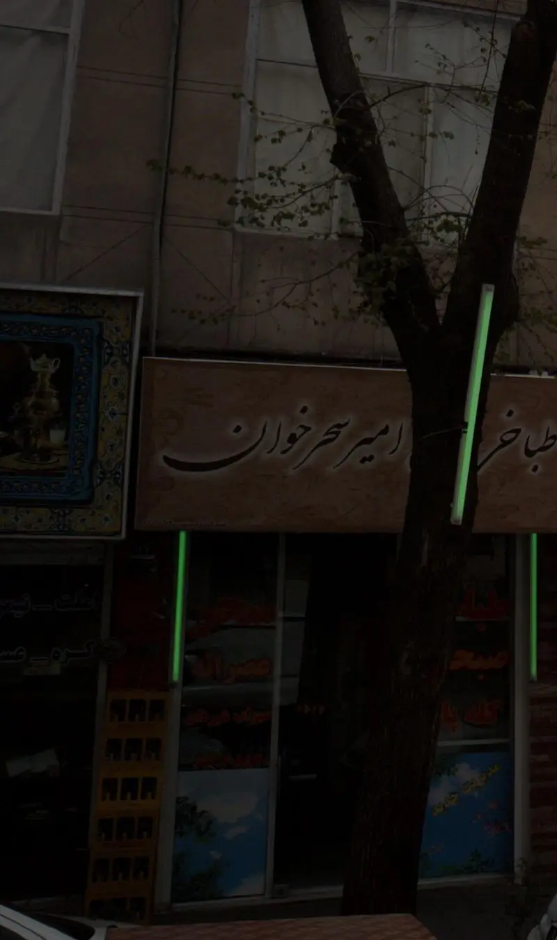 نمای بیرونی طباخی حاج امیر سحرخوان با تابلو روشن و درخت جلوی آن؛ یک کسب و کار سنتی ایرانی برای کله پاچه.