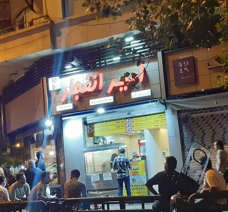 رستوران لقمه امیر انفجار (Amir Enfejar Loqmeh Restaurant) در شب، با تابلوی نئون روشن و مشتریانی که در حال خرید غذا هستند.