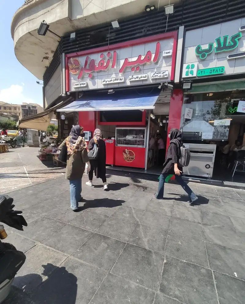 نمای بیرونی رستوران لقمه امیر انفجار با تابلوی قرمز و آبی در یک روز آفتابی، همراه با مشتریان و عابران در خیابان.