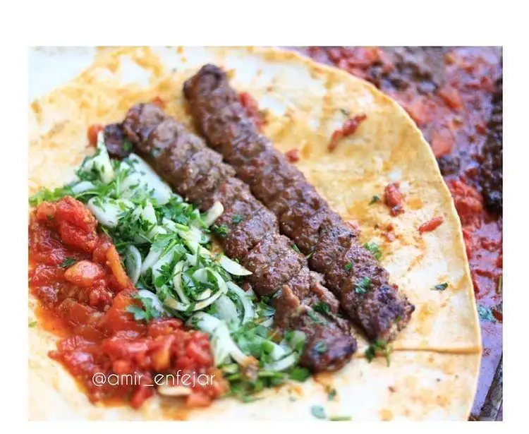 لقمه کباب کوبیده داغ و خوشمزه رستوران امیر انفجار، روی نان تازه با پیاز، جعفری و گوجه فرنگی، یک غذای خیابانی سنتی ایرانی.