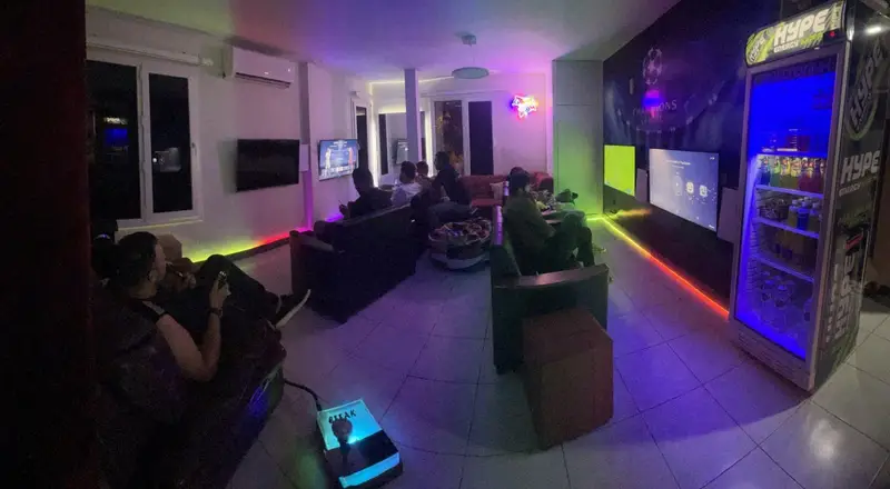 فضای داخلی گیم نت سورنا با بازیکنان در حال لذت بردن از بازی با PS5 و PS4، نورپردازی نئون، مبل‌های راحت و یخچال نوشیدنی پر از Hype Energy