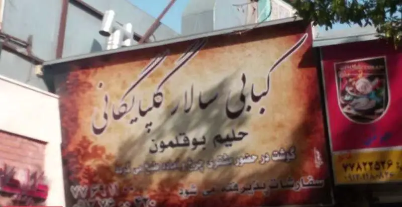 تصویر تابلوی کبابی سالار گلپایگان، ارائه دهنده کباب و حلیم بوقلمون، با تاکید بر چرخ کردن گوشت تازه در حضور مشتری و قبول سفارشات.