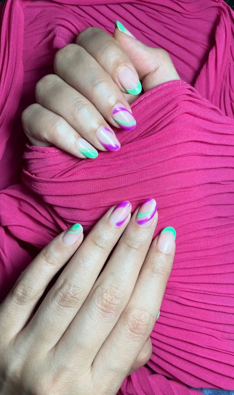 طراحی ناخن فانتزی و شیک دخترانه با لاک ژل سبز و بنفش به صورت خطوط منحنی و امواج روی پس زمینه پارچه پلیسه صورتی جذاب