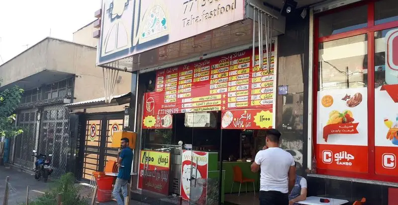 نمای بیرونی فست فود طاها با منوی کامل پیتزا، ساندویچ، سالاد و نوشیدنی‌ها، همراه با مشتریان و قیمت‌های به‌روز.