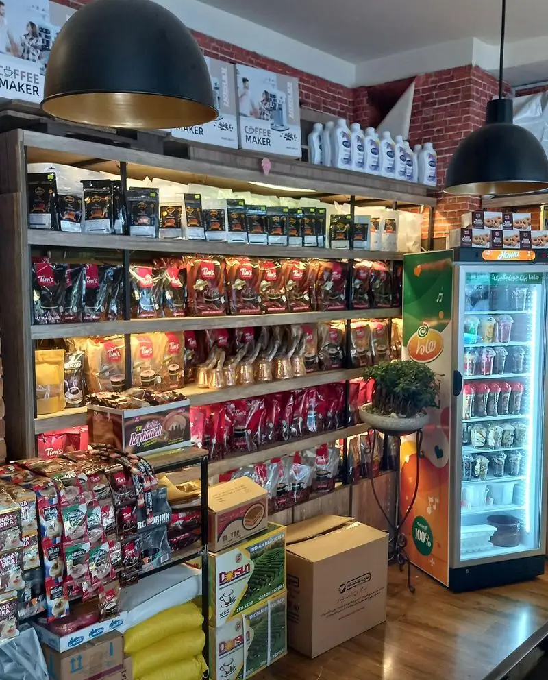 تصویری از فروشگاه قهوه کافی لند: قفسه‌های چوبی مملو از انواع قهوه، پودر قهوه، قهوه‌ساز و یخچال نوشیدنی.