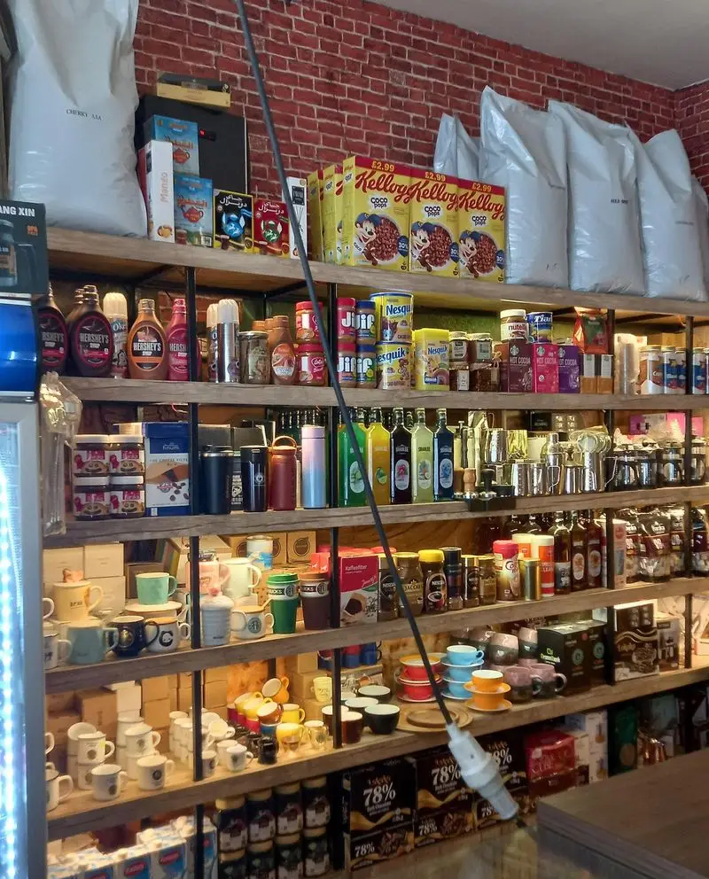 تصویری از قفسه‌های فروشگاه قهوه کافی لند با مجموعه‌ای غنی از دانه قهوه، انواع شربت، ماگ و لوازم جانبی کافه. مناسب برای عاشقان قهوه.
