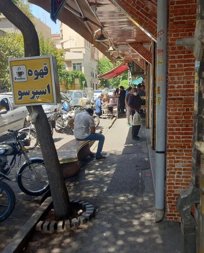 نمایی از خیابان با تابلوی قهوه و اسپرسو کافی لند، مشتریان در جلوی کافه نشسته و در حال خرید هستند در یک روز آفتابی.
