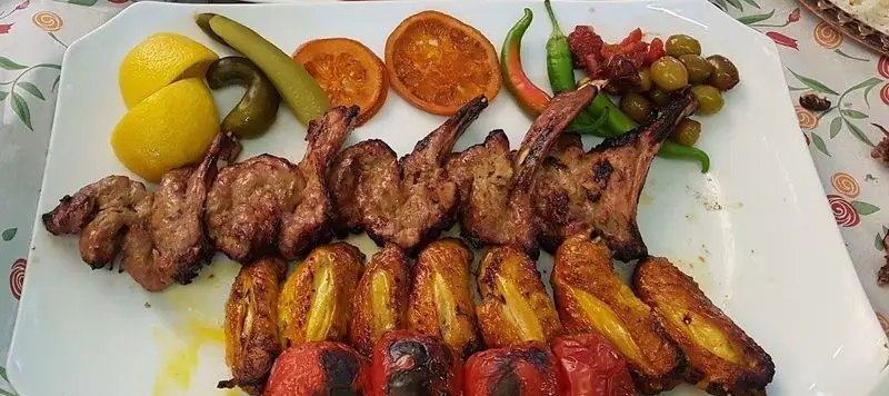 غذای لذیذ باغ رستوران نور: سینی کباب شیشلیک و جوجه کباب با گوجه کبابی، لیمو، زیتون، ترشیجات و فلفل تازه.