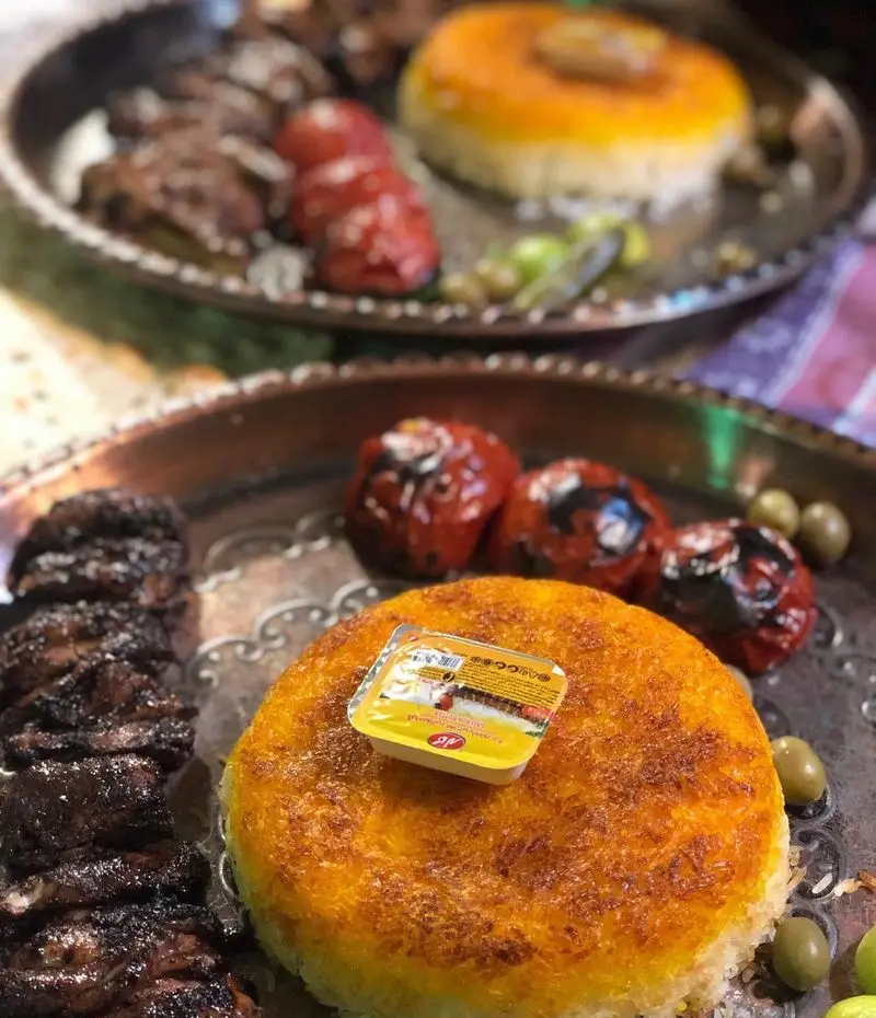 سینی غذای سنتی ایرانی شامل کباب، ته چین زعفرانی خوشرنگ با کره، گوجه کبابی و زیتون در باغ رستوران نور. یک تجربه خوشمزه.