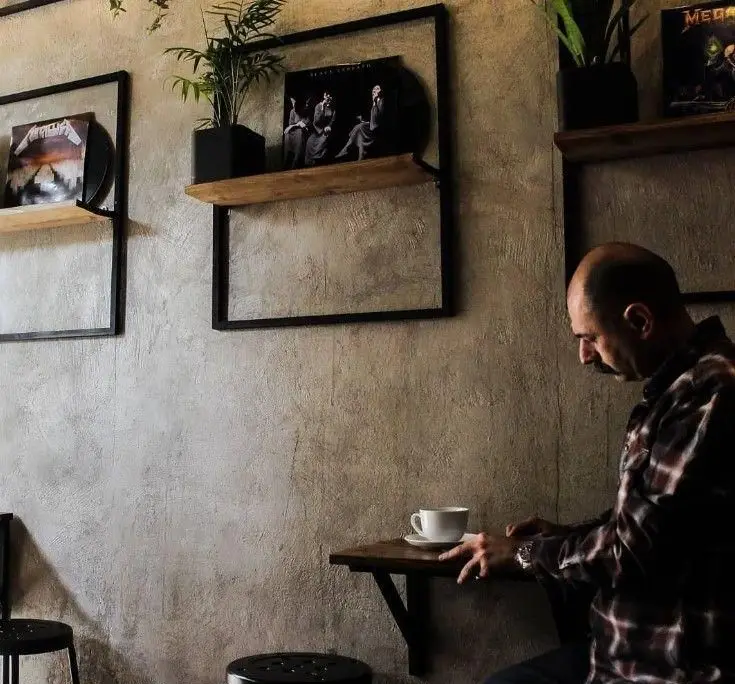 فضای دلنشین کافه گات با دکوراسیون صنعتی و قفسه‌های چوبی حاوی آلبوم‌های موسیقی راک مانند متالیکا و بلک سبث. مشتری در حال نوشیدن قهوه.