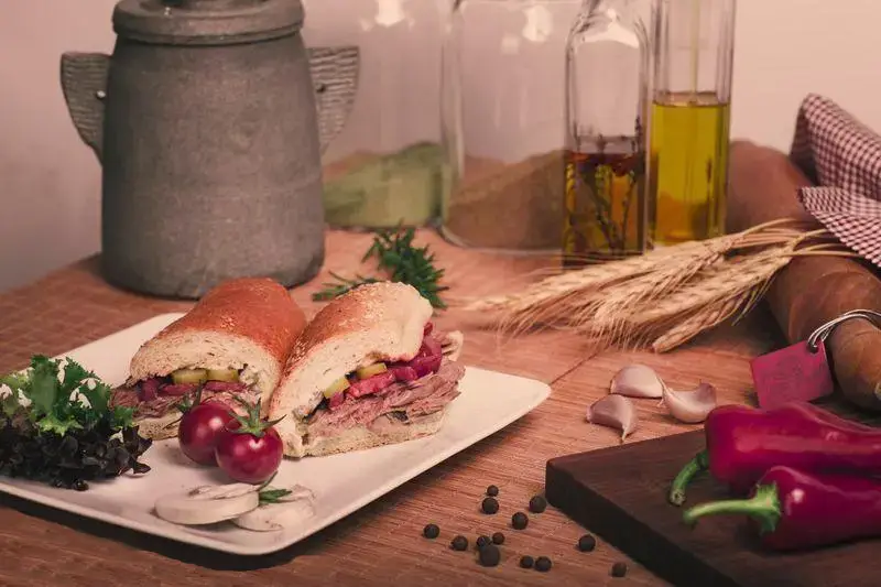 ساندویچ خانگی ویژه با گوشت تازه و نان باگت، همراه با ترشیجات و سبزیجات متنوع. نمایانگر طعم اصیل و سالم در محیطی گرم و دلپذیر.