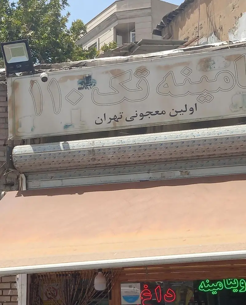 عکس تابلوی مغازه ویتامینه تک ۱۱۰، اولین معجونی در تهران. دارای سایبان نارنجی و نورپردازی نئون "ویتامینه داغ".