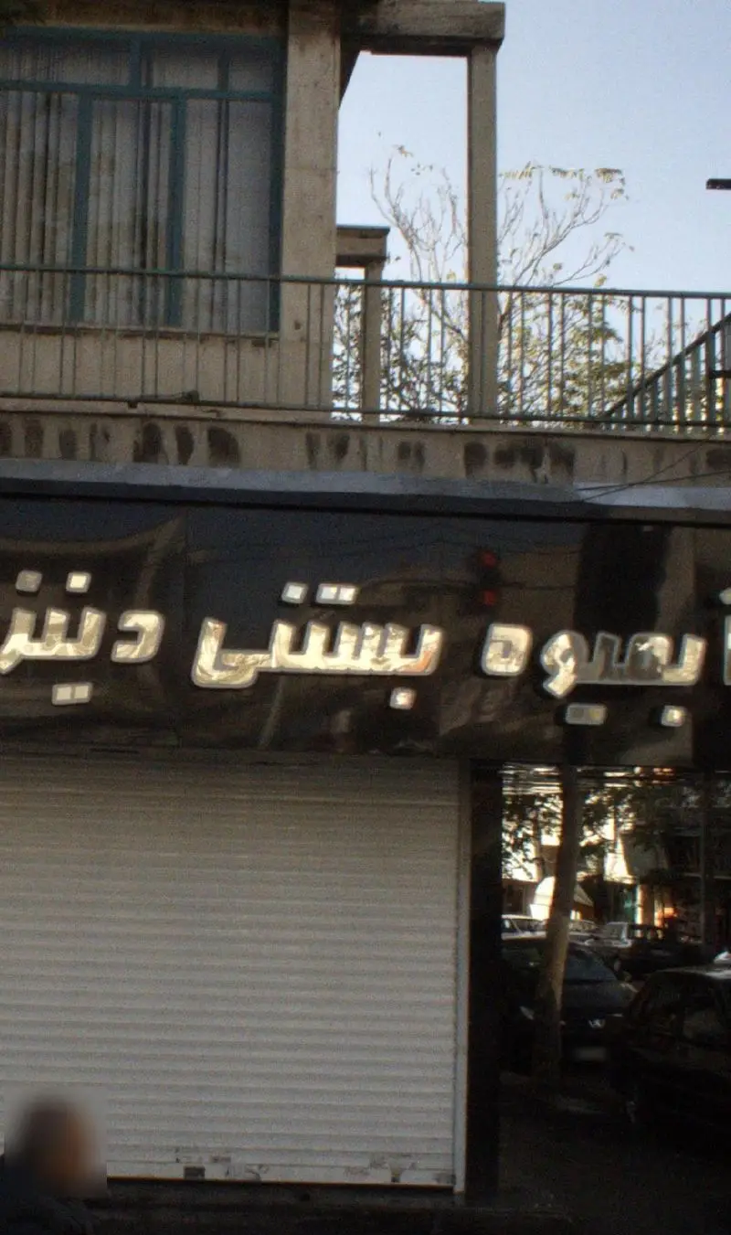 نمای جلوی فروشگاه آبمیوه بستنی دنیز، با تابلوی روشن و حروف نقره‌ای برجسته روی پس‌زمینه مشکی، کرکره مغازه بسته است.