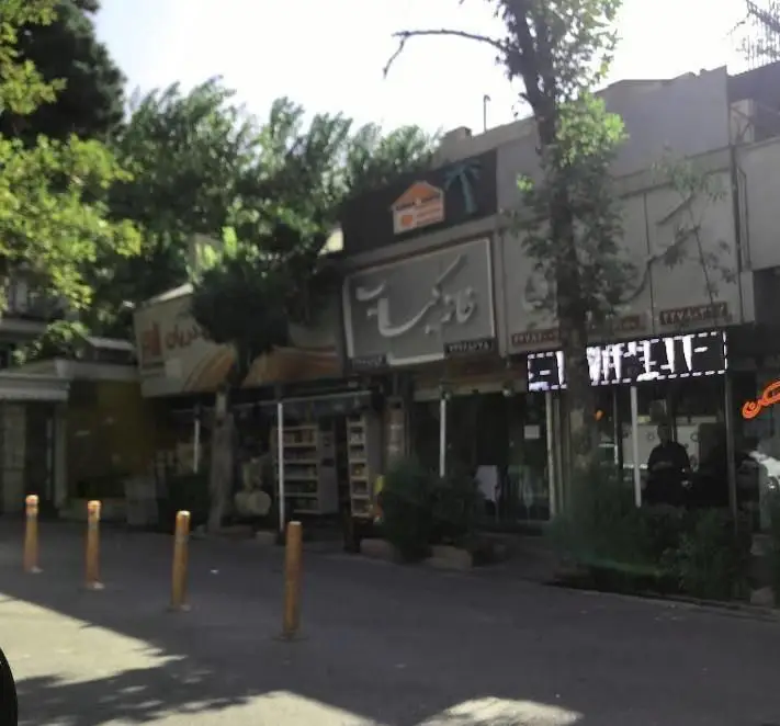 نمای بیرونی رستوران "کبابی خانه کباب" در کنار خیابان، با تابلوهای روشن، درختان سرسبز و محیطی آرام. مناسب برای لذت بردن از کباب‌های اصیل ایرانی.