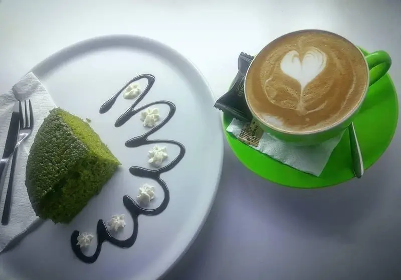 دسر لذیذ کیک سبز همراه با قهوه لاته آرت خاص کافه مانژه. تجربه‌ای شیرین و دلپذیر از منوی بی‌نظیر کافه.