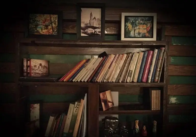 کتابخانه دنج و هنری کافه مانژه با ردیفی از کتاب‌ها و تابلوهای زیبا، فضایی دلنشین برای مطالعه و آرامش.