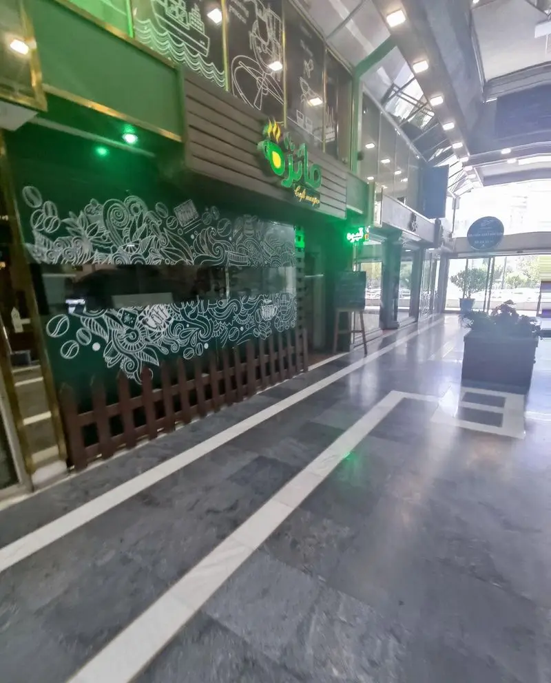 نمای جذاب کافه مانژه با دکوراسیون سبز، طرح‌های هنری سفید، تابلوی مشخص و ورودی دعوت‌کننده برای انواع نوشیدنی و قهوه.