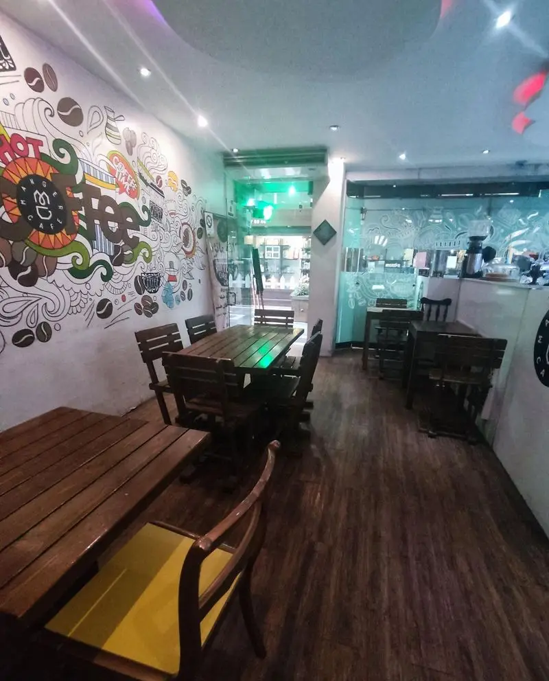 فضای داخلی دنج کافه مانژه با دیوارنگاری هنری قهوه، میز و صندلی‌های چوبی مدرن و محیطی دلنشین برای مشتریان.