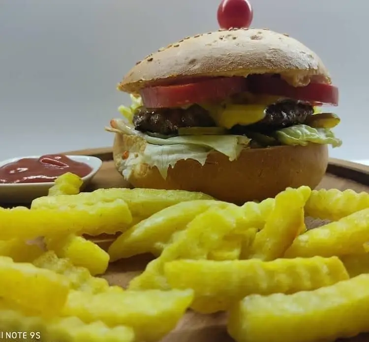 عکس همبرگر مخصوص کافه مانژه شامل برگر گوشت، پنیر، کاهو و گوجه فرنگی، همراه با سیب زمینی سرخ کرده کرانچی و سس کچاپ برای یک وعده غذایی لذیذ.
