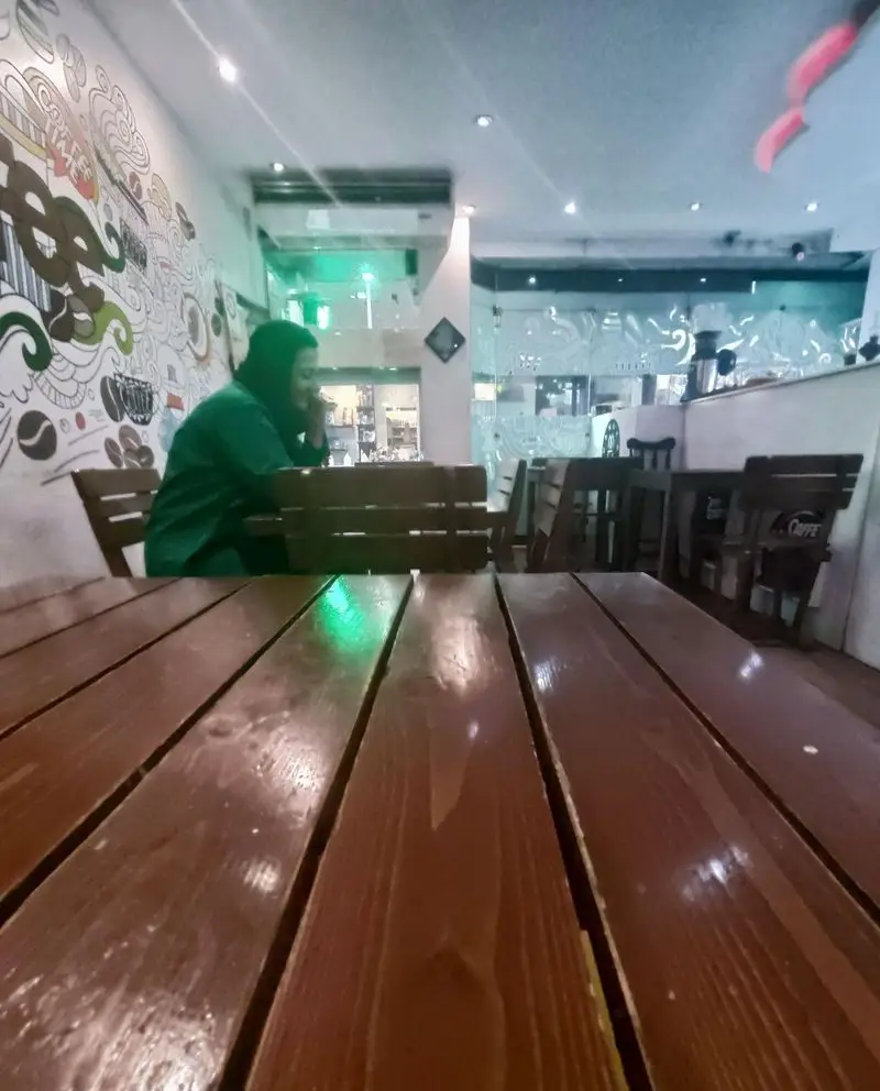 فضای داخلی دنج کافه مانژه با دکوراسیون جذاب، میزهای چوبی براق، و مشتری در حال لذت بردن از محیط آرام. انتخابی عالی.