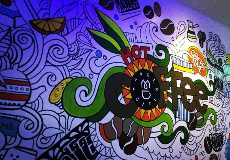 تصویری از دیوارنگاری هنری و رنگارنگ در کافه مانژه با شعار "HOT COFFEE"، شامل لوگوی کافه و عناصر جذاب مرتبط با قهوه، دکوراسیون داخلی.
