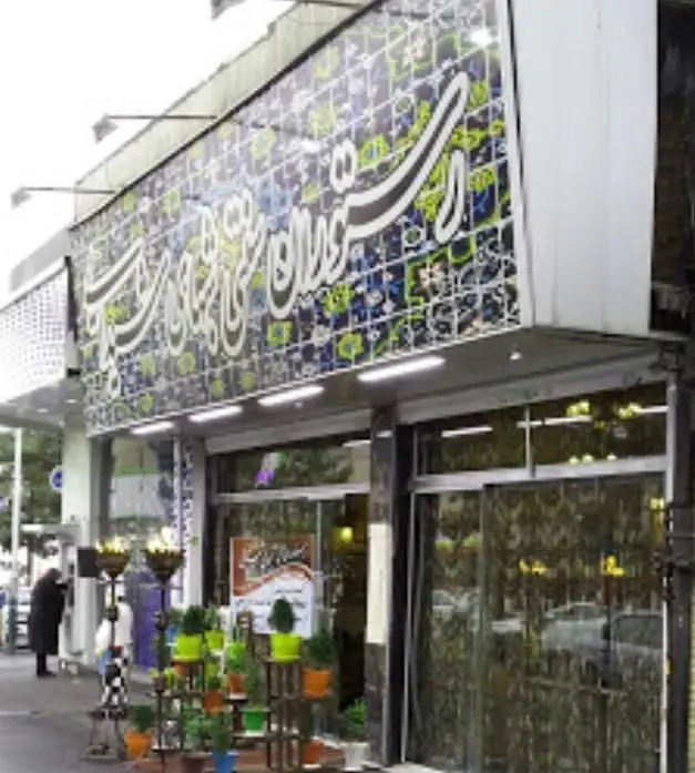 تصویری از نمای بیرونی و سردر یک سفره خانه سنتی به نام شب های شیدایی با تابلوی بزرگ و خطاطی برجسته، نورپردازی زیبا و گلدان‌های تزئینی در پیاده‌رو.