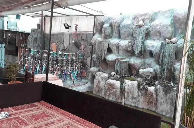 سفره خانه سنتی شب های شیدایی: فضایی آرامش‌بخش با آبنما سنگی، تخت‌های سنتی و مجموعه‌ای از قلیان‌های آماده برای سرو.