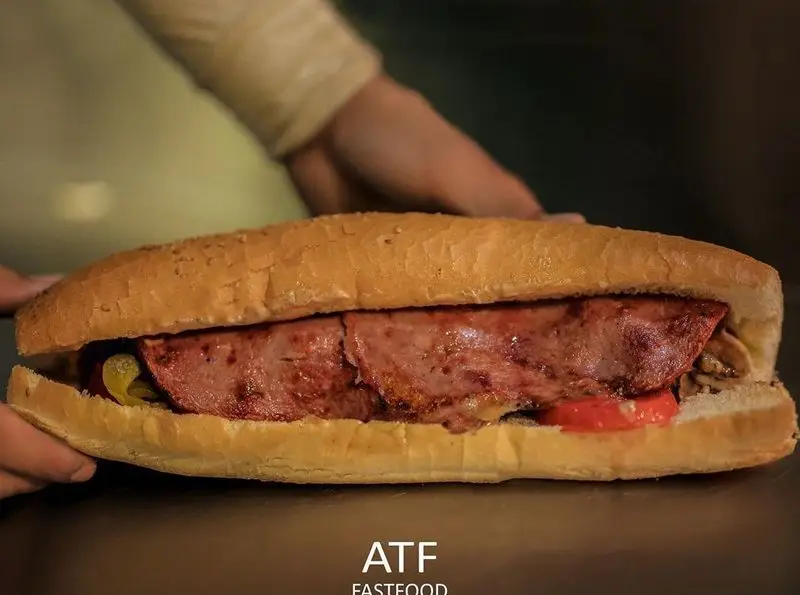 ساندویچ بزرگ و خوشمزه رستوران ای تی اف با سوسیس گریل شده، نان باگت، فلفل ترشی و گوجه فرنگی تازه. فست فود لذیذ.