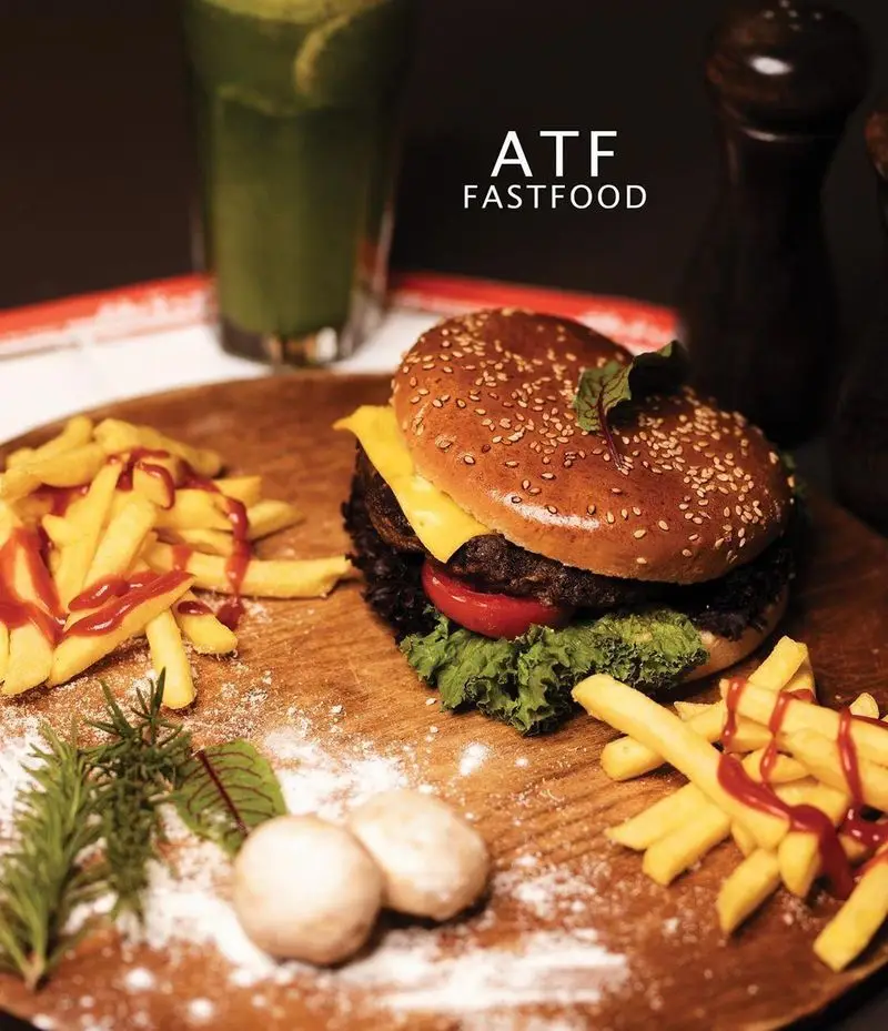 همبرگر خوشمزه با پنیر، کاهو و گوجه، در کنار سیب زمینی سرخ کرده با سس کچاپ و نوشیدنی خنک در رستوران فست فود ATF.