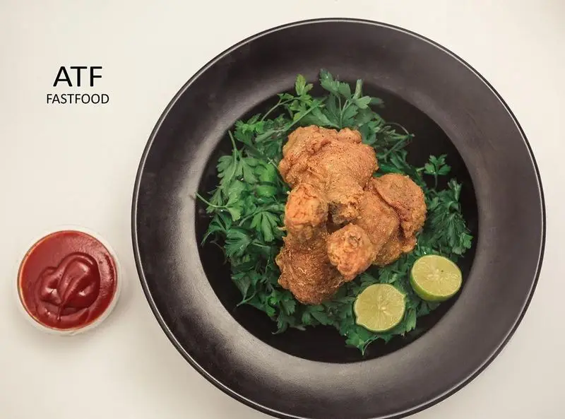 تصویر مرغ سوخاری خوشمزه رستوران ATF Fastfood در بشقاب مشکی همراه با سبزیجات تازه، دو برش لیمو و سس کچاپ قرمز.