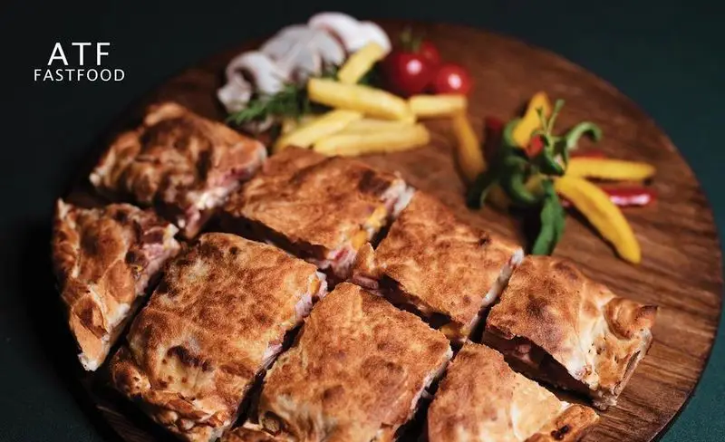 غذای فست فود رستوران ATF FASTFOOD: پای گوشت و پنیر گرم و خوشمزه، برش خورده و آماده سرو، همراه با سیب زمینی سرخ کرده و گوجه گیلاسی.