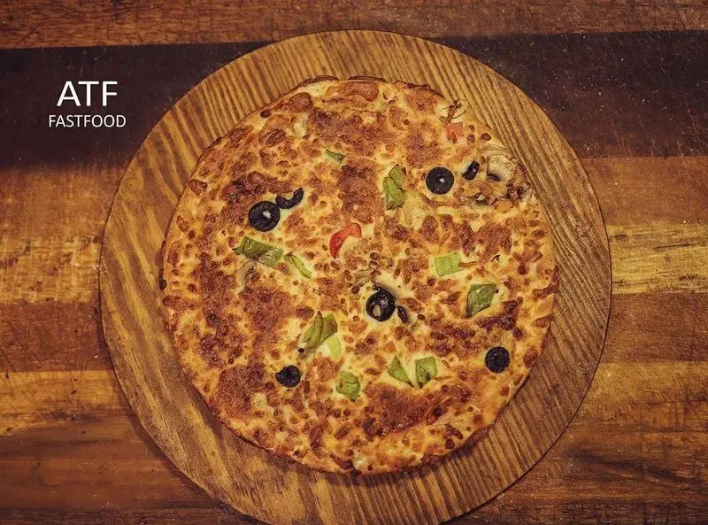 پیتزا رستوران ای تی اف با پنیر طلایی، زیتون، فلفل دلمه‌ای سبز و قرمز روی سینی چوبی. غذای فست فود خوشمزه ATF.