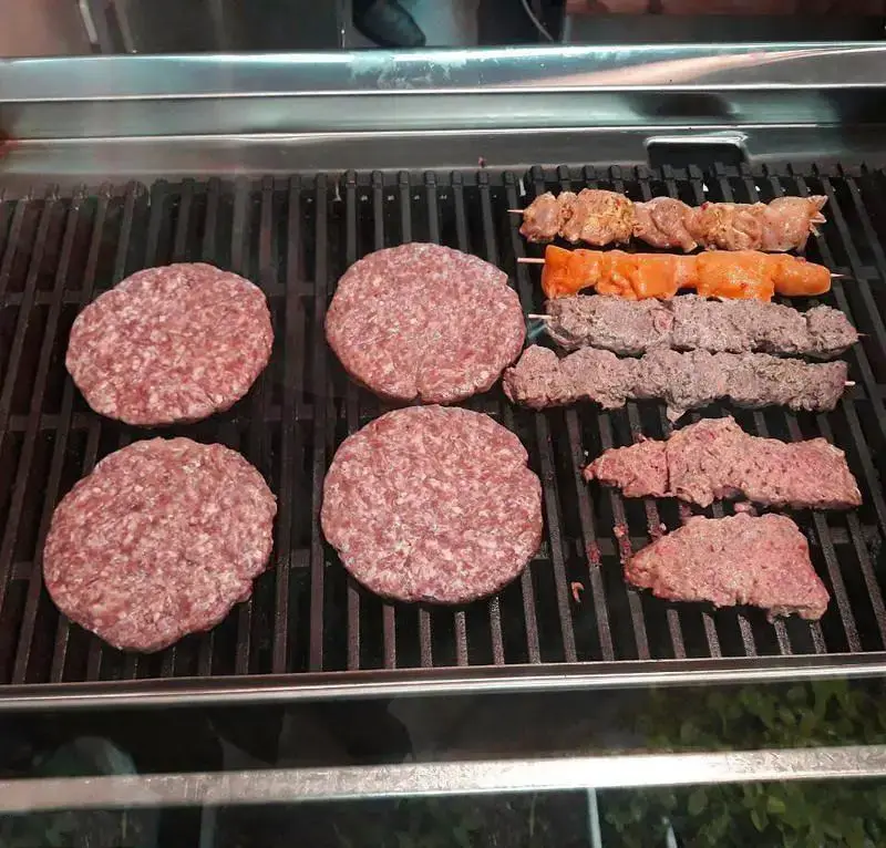 چهار برگر گوشت ارگانیک و کباب‌های تازه (شامل کوبیده و جوجه) روی گریل، آماده طبخ در "برگر ارگانیک برگر".