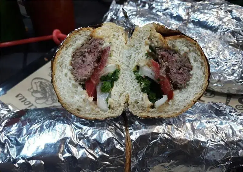 تصویر کلوزآپ برگر ارگانیک تازه و آبدار با گوشت دست‌ساز، گوجه، پیاز و سبزیجات معطر، از وسط برش خورده و آماده سرو در فویل.