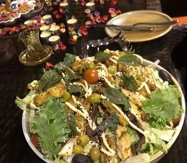 سالاد مرغ و سبزیجات تازه با زیتون و سس در کافی شاپ پرسیس، روی میزی تزیین شده با شمع و چای برای تجربه ای دلنشین.