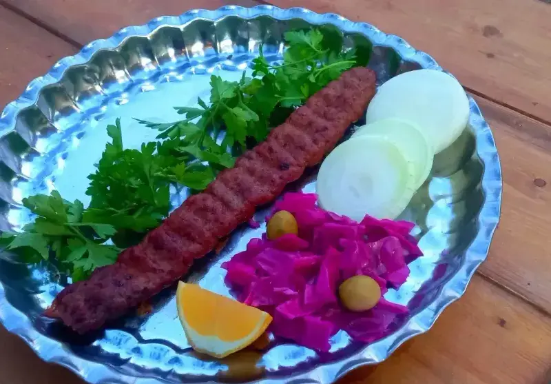 بشقاب کباب کوبیده آبدار کبابسرای عشاق با دورچین جعفری، پیاز حلقه ای، کلم بنفش و پرتقال. تجربه طعم اصیل غذای سنتی ایرانی.