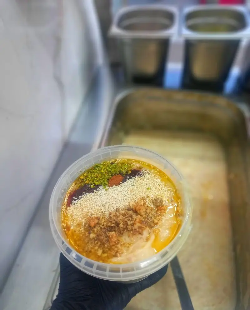 یک ظرف دسر شیرین و مقوی از کبابسرای عشاق با پسته، کنجد، گردو و شیره، آماده سرو در محیط آشپزخانه.