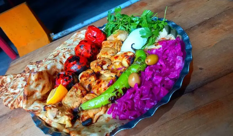 سینی جوجه کباب مخصوص کبابسرای عشاق با گوجه کبابی، فلفل، ترشی کلم بنفش، جعفری، زیتون و نان تازه، یک غذای اصیل ایرانی