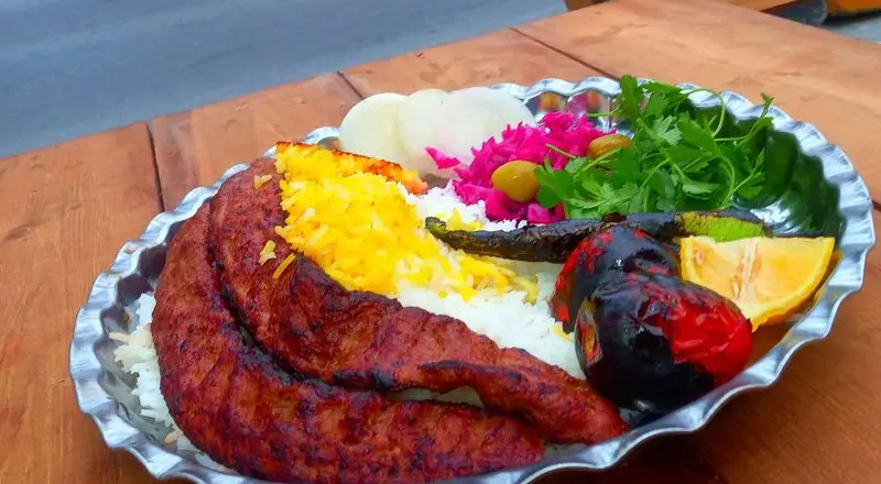 بشقاب کباب کوبیده کبابسرای عشاق با برنج زعفرانی، گوجه و فلفل کبابی، پیاز، زیتون و سبزیجات تازه. یک غذای سنتی و خوشمزه ایرانی.