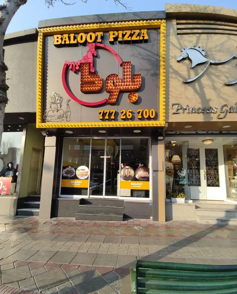 تصویر نمای بیرونی رستوران فست فود پیتزا بلوط، با تابلوی بزرگ، نام فارسی و انگلیسی، و شماره تماس 77726700.