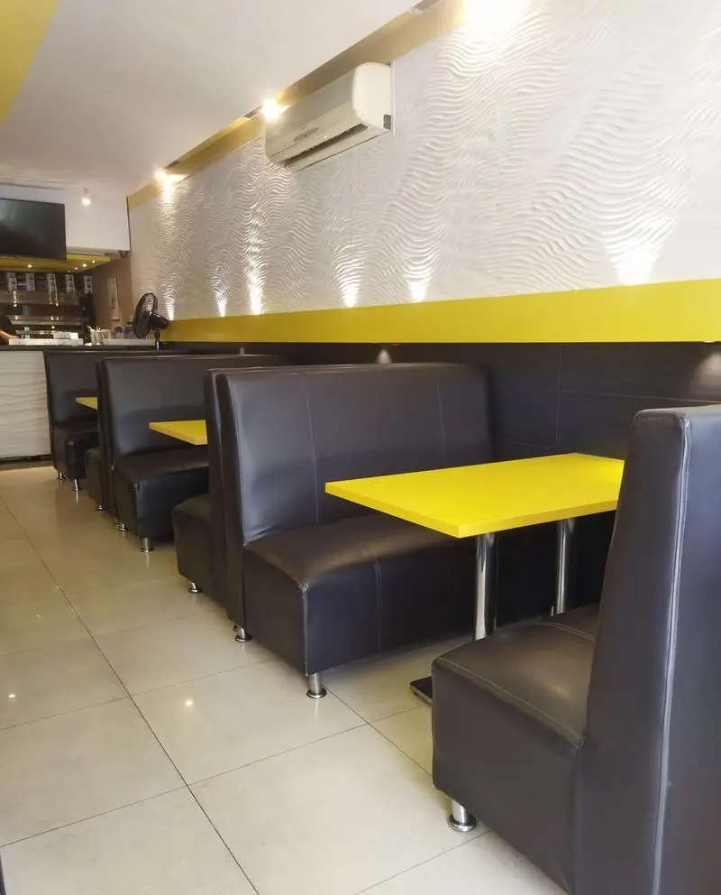 فضای داخلی فست فود بلوط با میزهای زرد و صندلی‌های چرم تیره و دیوار طرح‌دار سفید، محیطی مدرن و راحت برای مشتریان