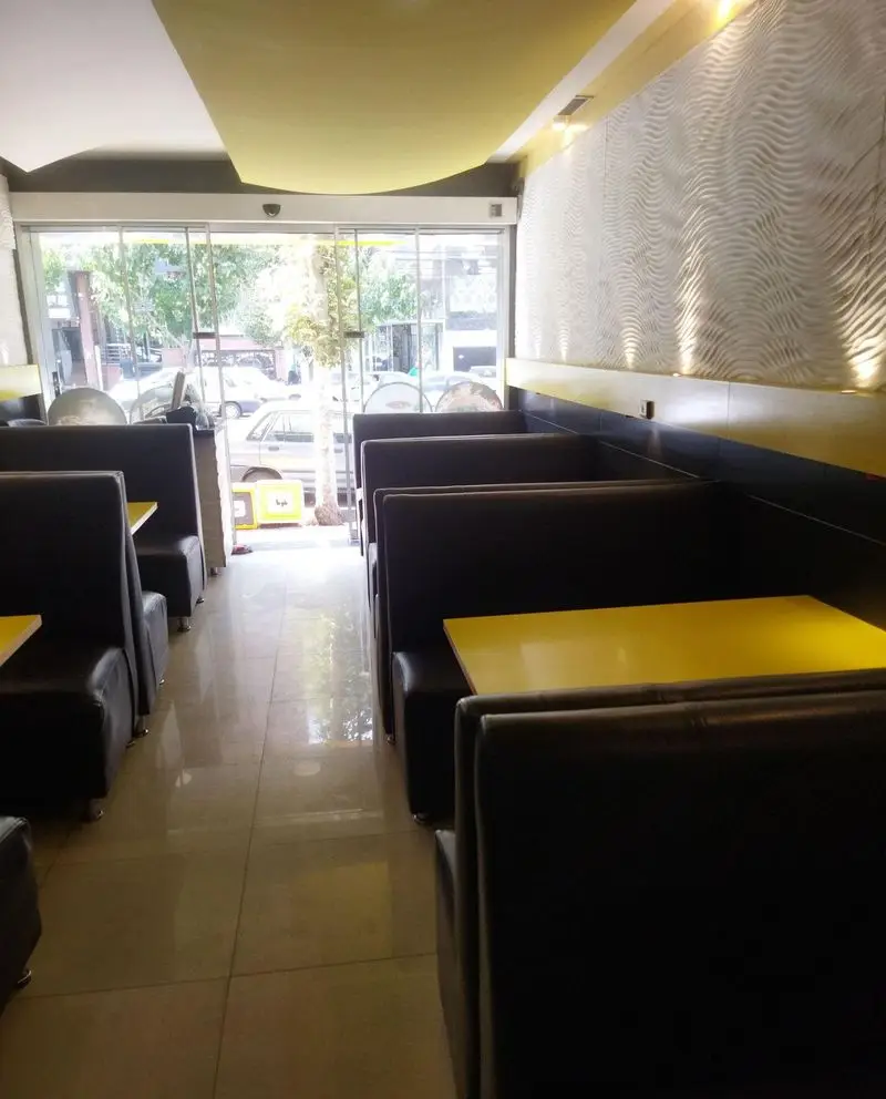 فضای داخلی فست فود بلوط با میزهای زرد و صندلی های مشکی، دکوراسیون مدرن و نورپردازی زیبا مناسب برای تجربه غذایی لذت بخش.